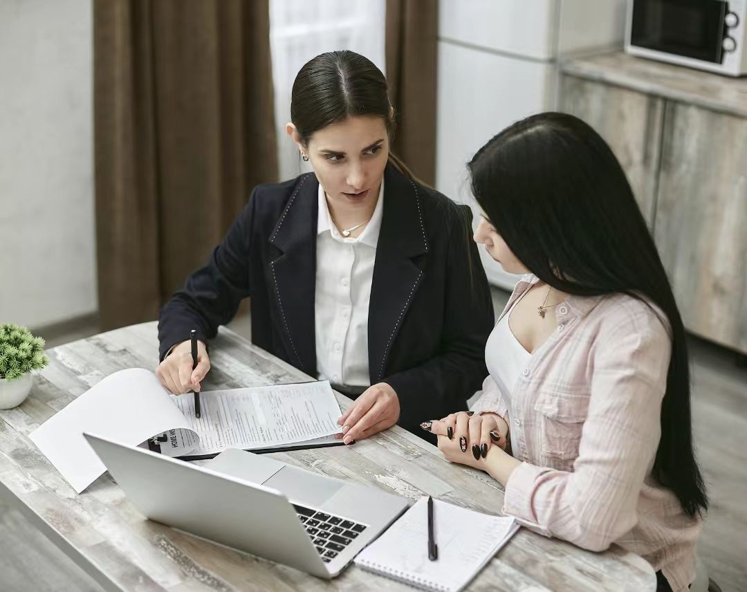 Two women collaborating on work at a laptop and documents.